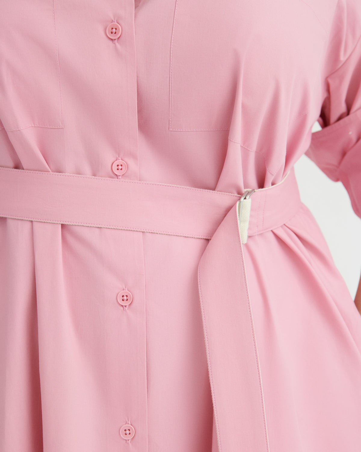 Close-up of a pink belted shirt dress with matching buttons, showing the waist tie and fabric texture.