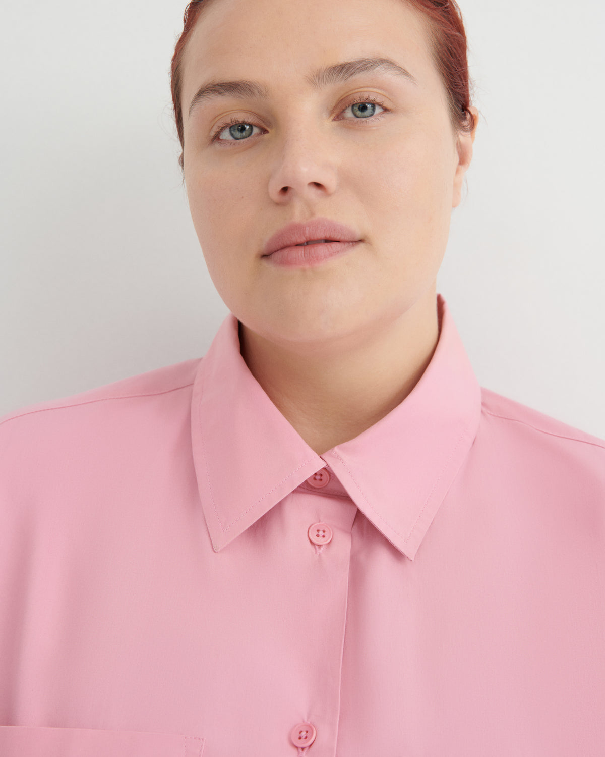 A close-up shot of a model wearing a light pink button-down shirt with a classic collar.