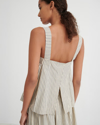 A woman shown from the back wearing a sleeveless striped dress with wide shoulder straps and a tiered ruffled overlay, photographed against a plain light gray studio background.