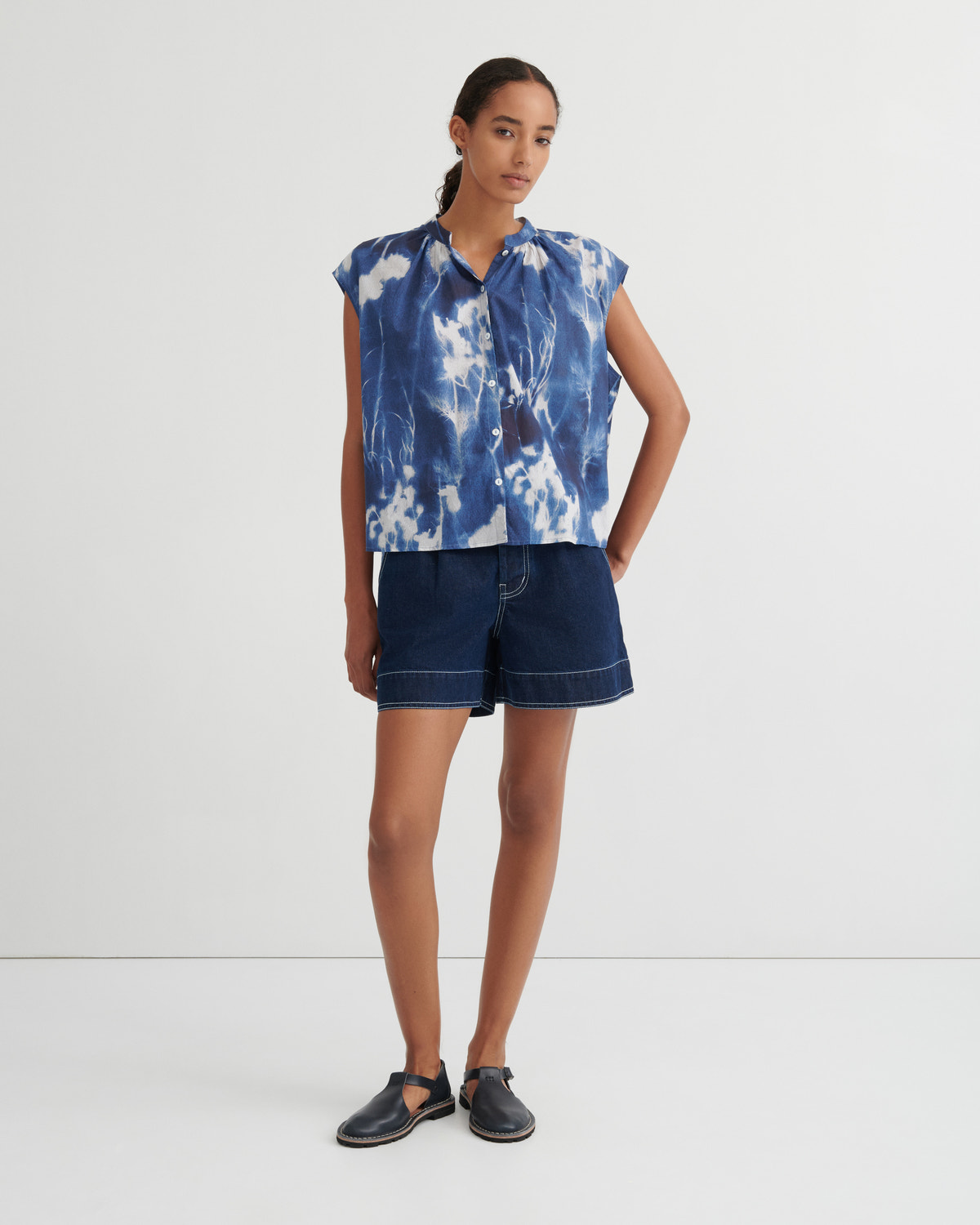 Woman wearing a blue tie-dye top and denim shorts on a white background
