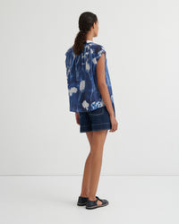 Woman wearing a blue tie-dye shirt and denim shorts on a white background