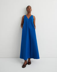 A model wearing a sleeveless, V-neck maxi dress in a vibrant royal blue, paired with brown leather shoes, standing against a plain white studio background.