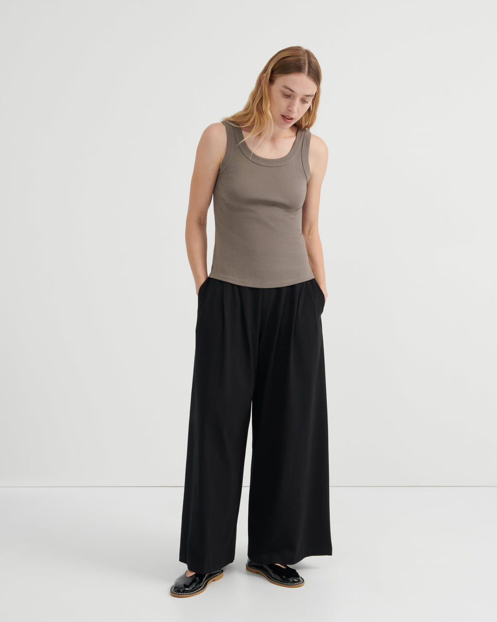 A woman modeling a sleeveless taupe ribbed tank top and black wide-leg trousers.