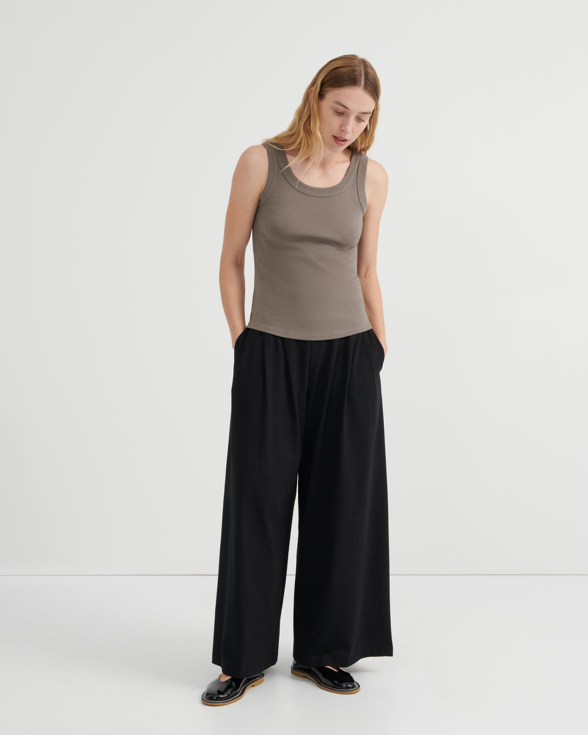 A woman modeling a sleeveless taupe ribbed tank top and black wide-leg trousers.