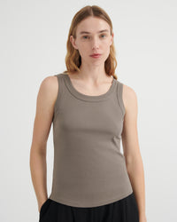 A woman modeling a sleeveless scoop-neck tank top in a muted taupe-brown color, paired with a black skirt.