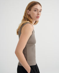 A woman shown in side profile wearing a fitted sleeveless top in a muted taupe-gray color, paired with black bottoms.