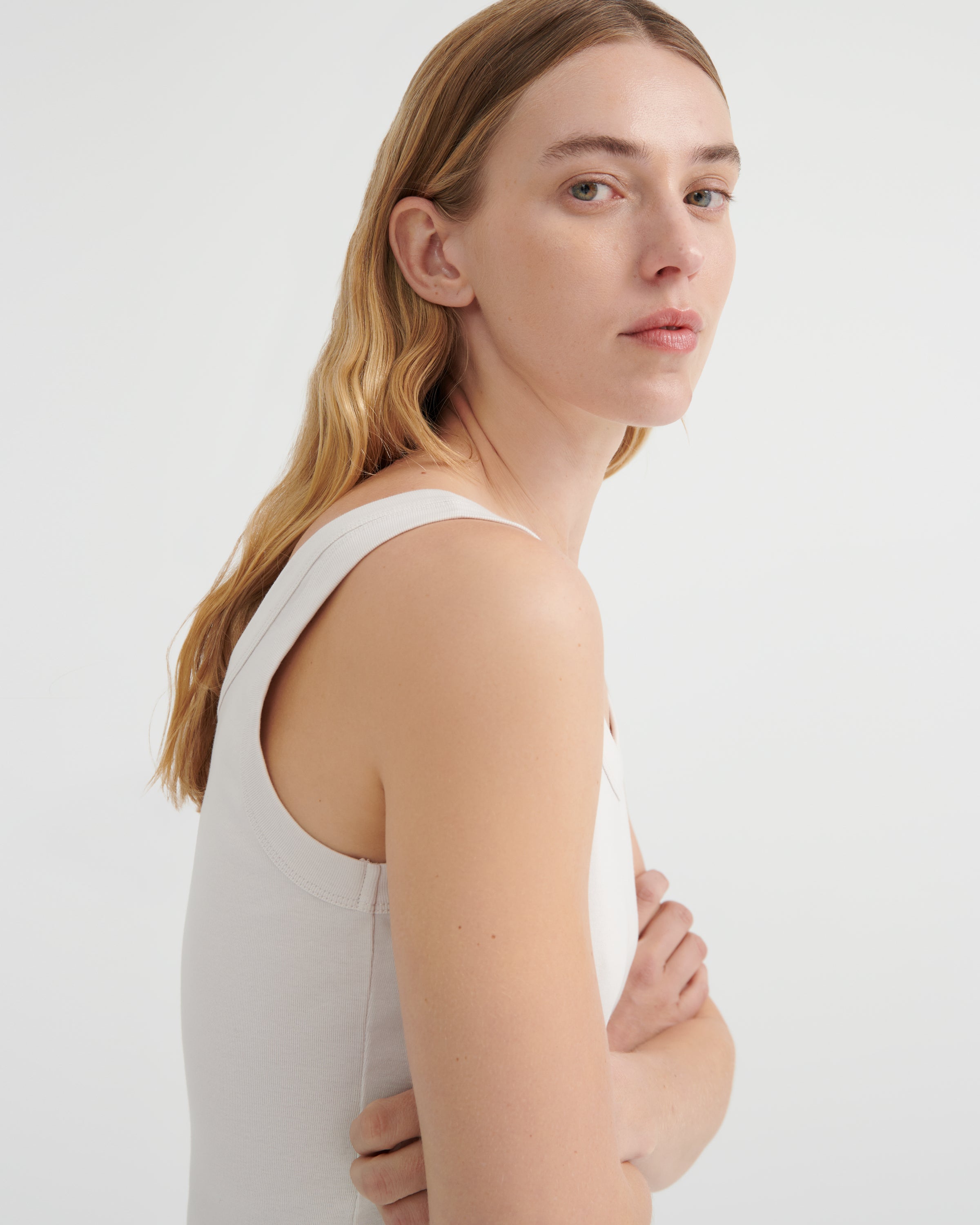 A woman is shown from a side-back angle wearing a light beige sleeveless tank top.