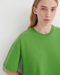 A close-up of a model wearing a bright green crewneck t-shirt against a plain light gray background.
