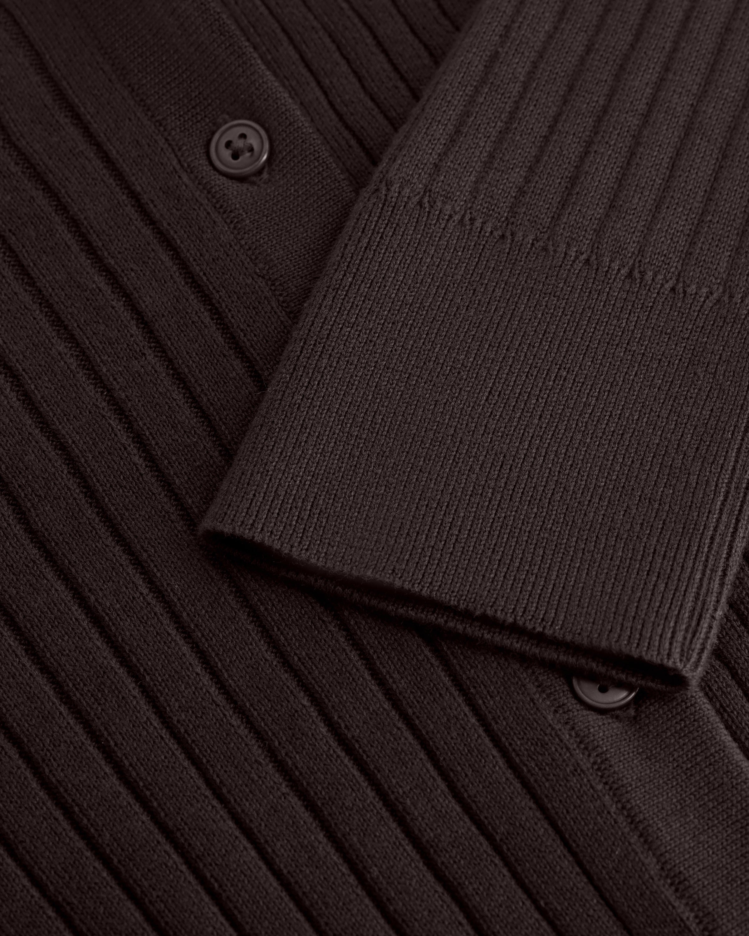 Close-up of a dark brown ribbed knit cardigan or sweater showing the sleeve cuff, button detail, and textured fabric.