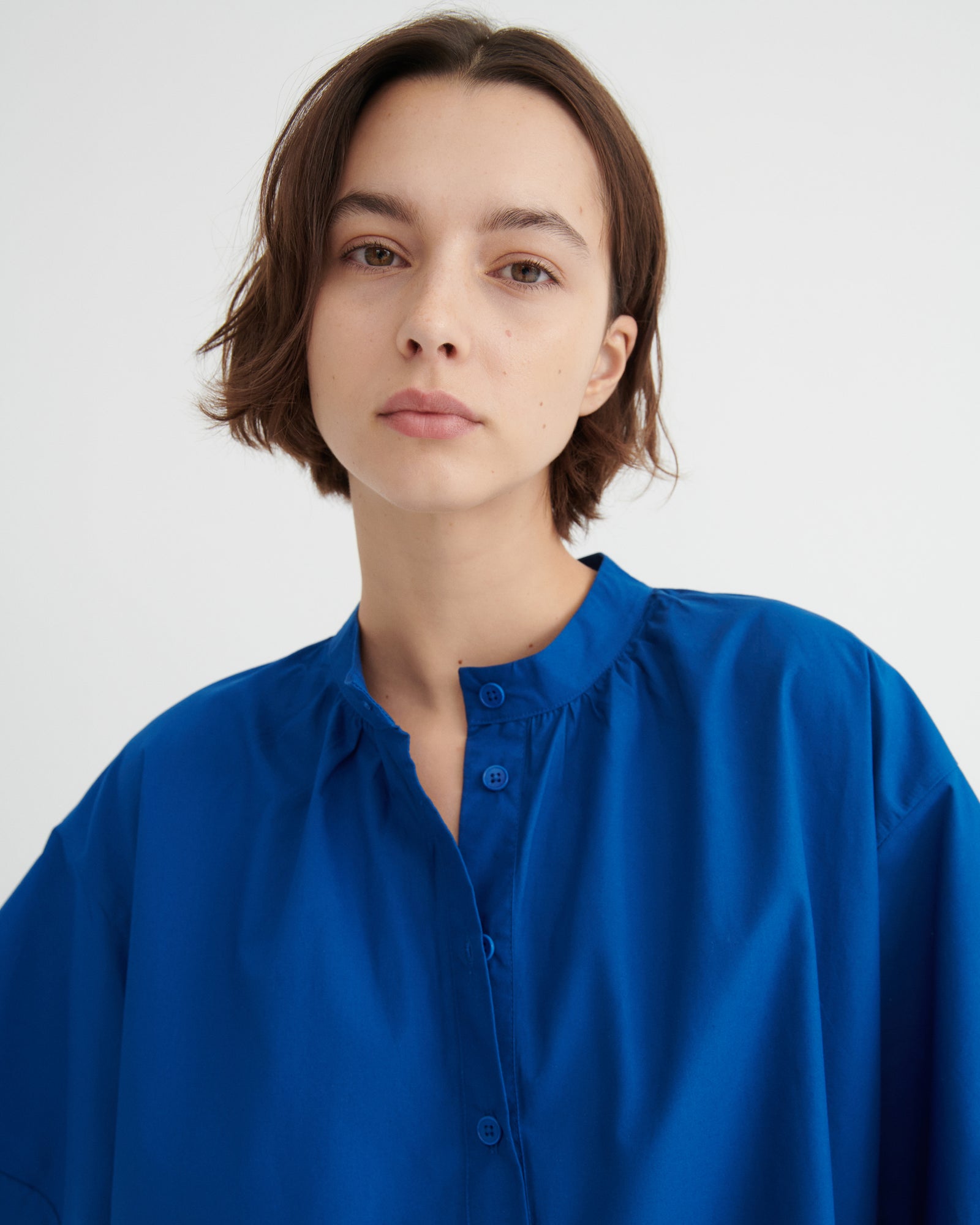 A woman with short brown hair wearing a vibrant royal blue button-up dress.
