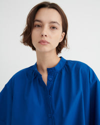 A woman with short brown hair wearing a vibrant royal blue button-up dress.