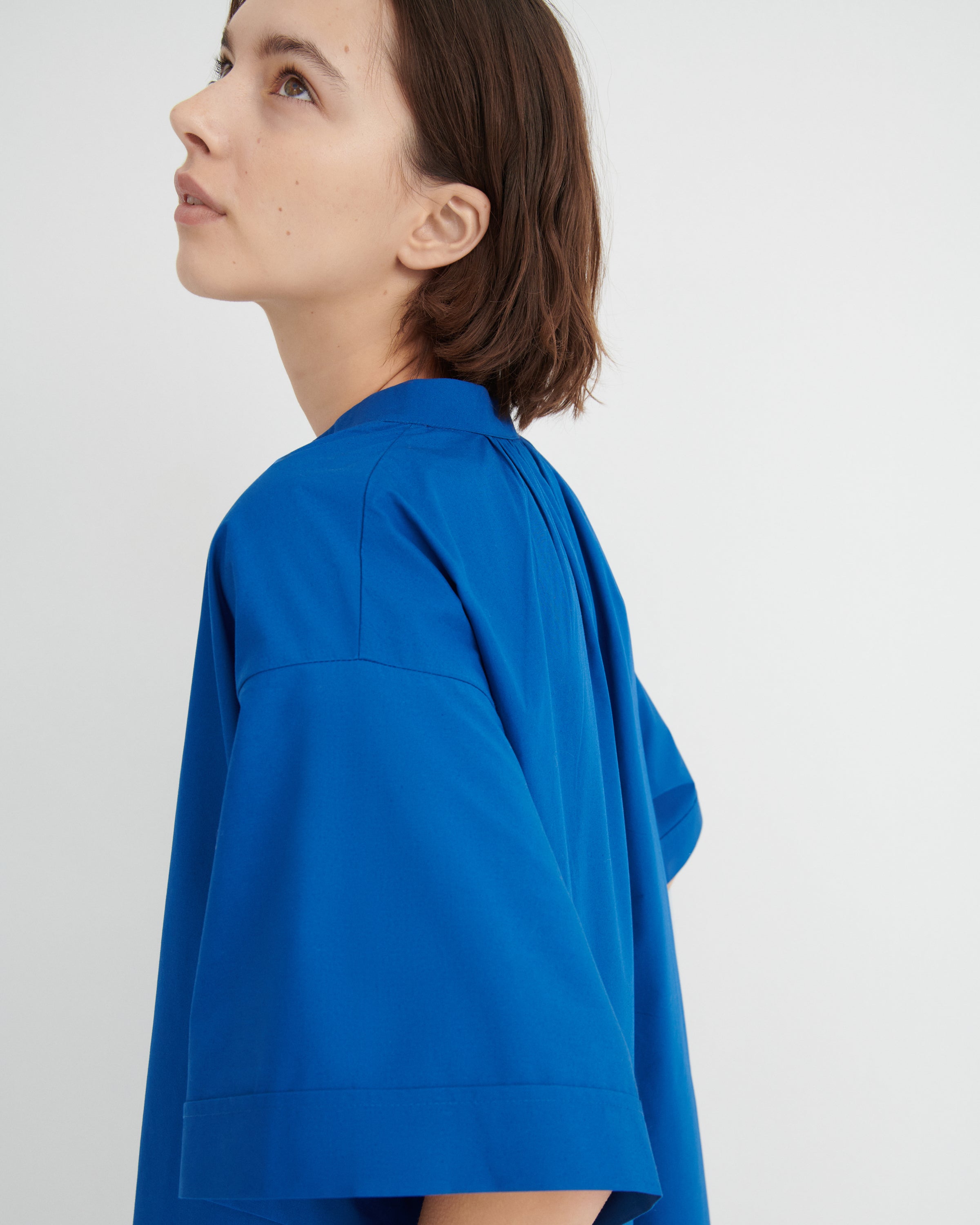 A woman shown in profile wearing a bright royal blue short-sleeve dress.