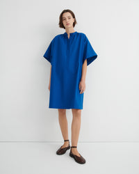 A woman modeling a loose-fitting, short-sleeved blue dress with a buttoned mock neck.
