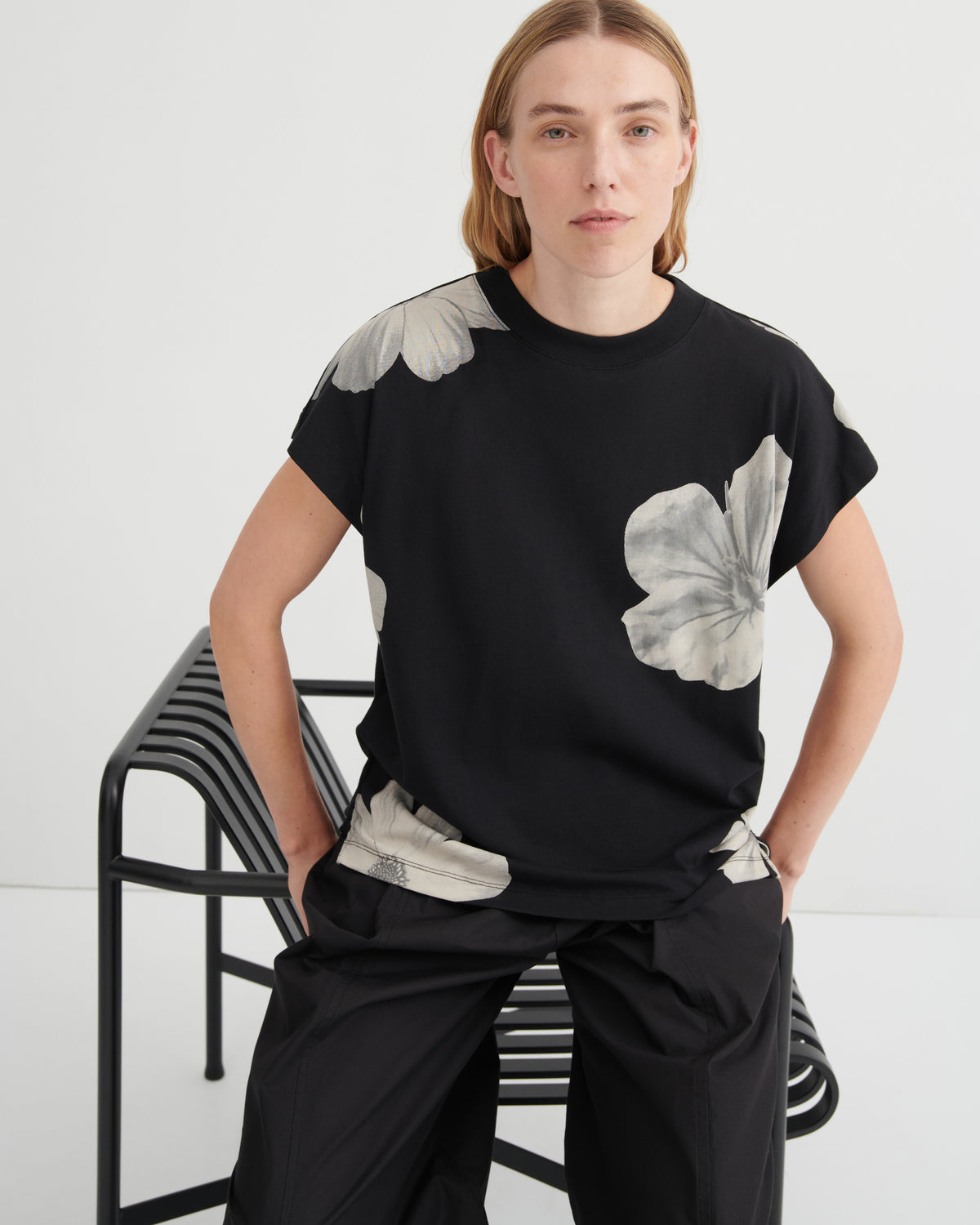 Person wearing a black t-shirt with floral designs sitting on a chair against a white background