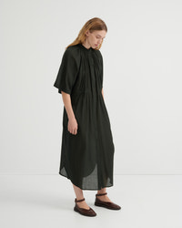 A woman modeling a loose, olive green midi dress with short flutter sleeves, a gathered high neckline, and a draped silhouette, paired with dark brown flat shoes against a plain white studio background.