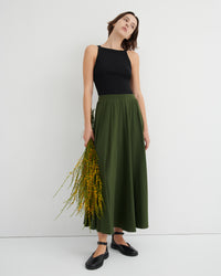 Woman wearing a black top and green skirt holding flowers against a white background