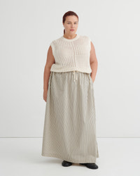 A woman modeling a cream sleeveless knit top paired with a beige and white vertically striped maxi skirt, standing against a plain white studio background.