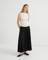 A woman modeling a sleeveless white ribbed knit top and a long black skirt, paired with black flat shoes.