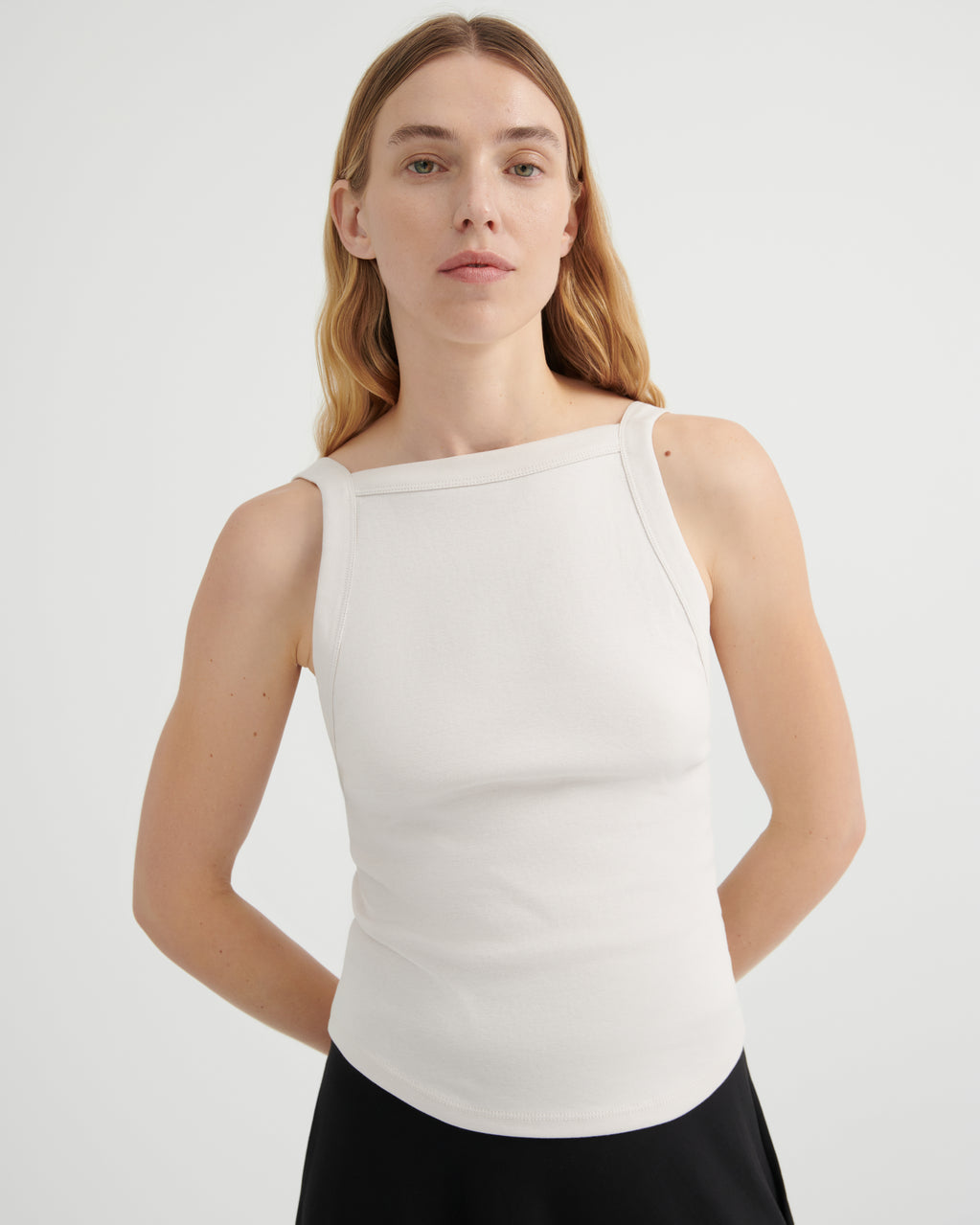 A woman modeling a fitted sleeveless top with a wide boat neckline.
