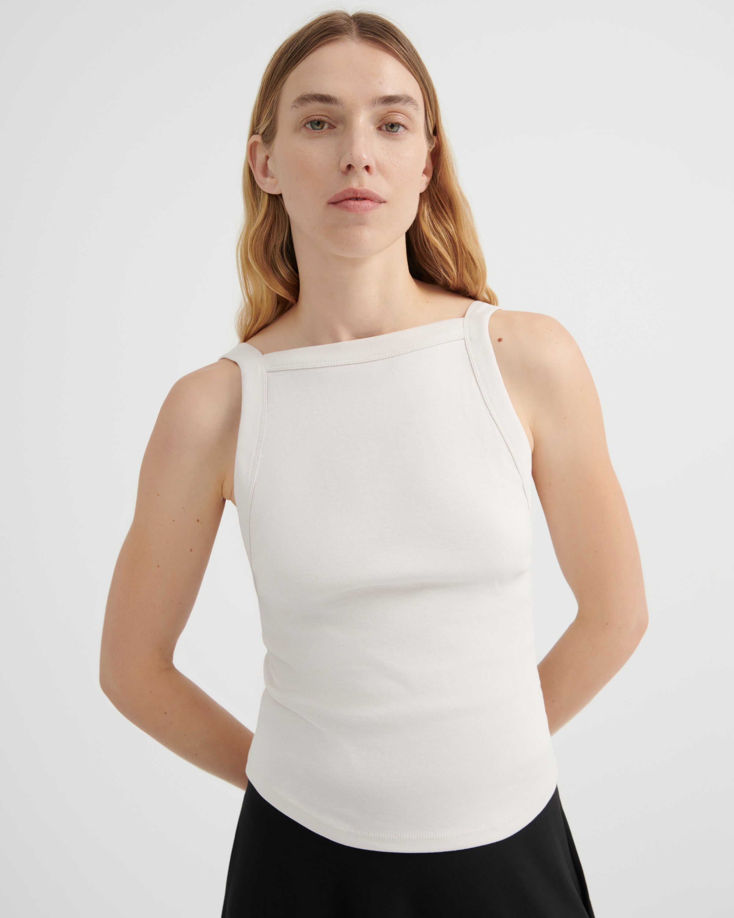 A woman modeling a fitted sleeveless top with a wide boat neckline.