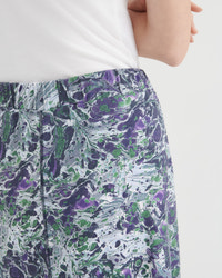 Close-up of a person wearing patterned skirt with an abstract marbled print in purple, green, black, and white, paired with a white top against a light gray background.