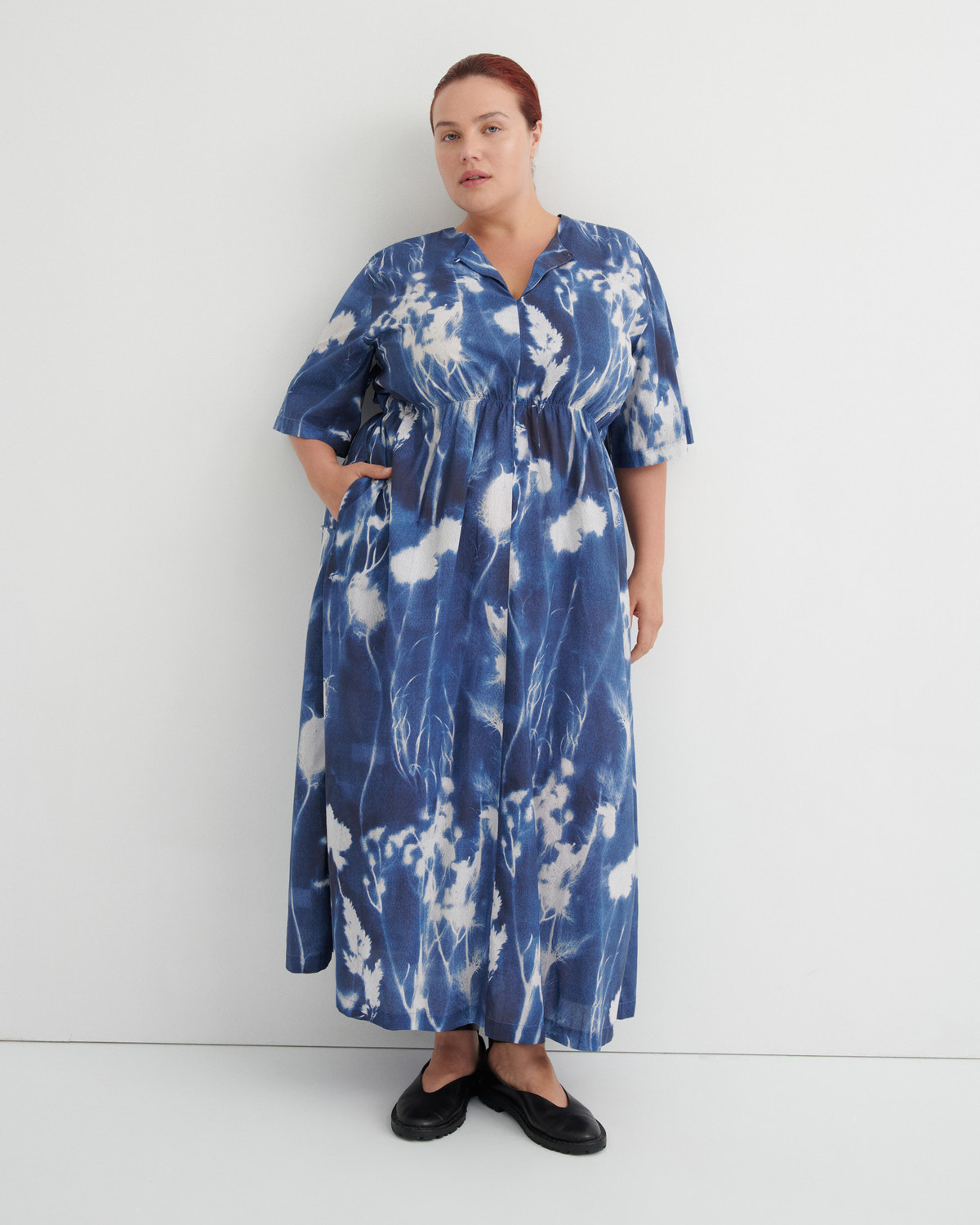 A woman modeling a blue and white tie-dye maxi dress with short flutter sleeves, a V-neck, and a drawstring waist, standing against a plain white studio background.