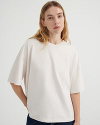 A woman wearing an oversized off-white short-sleeve crewneck t-shirt, paired with dark blue jeans.