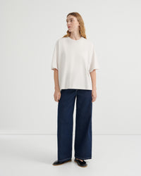 A woman wearing an oversized off-white short-sleeve top, dark blue wide-leg jeans, and black loafers.