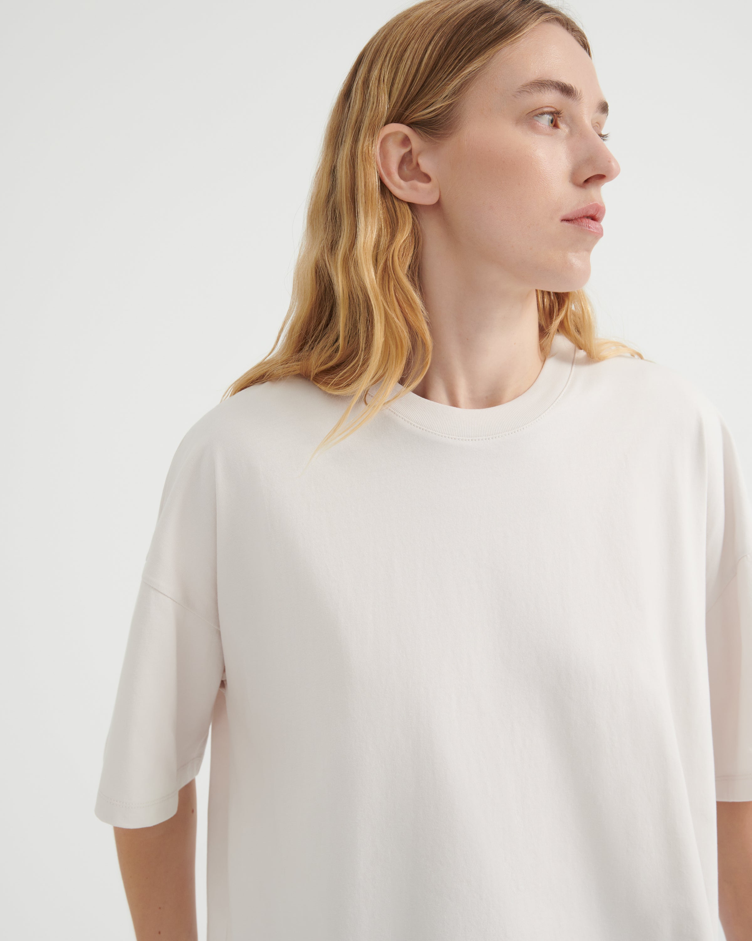 A woman wearing an oversized off-white crewneck t-shirt, shown from the chest up.