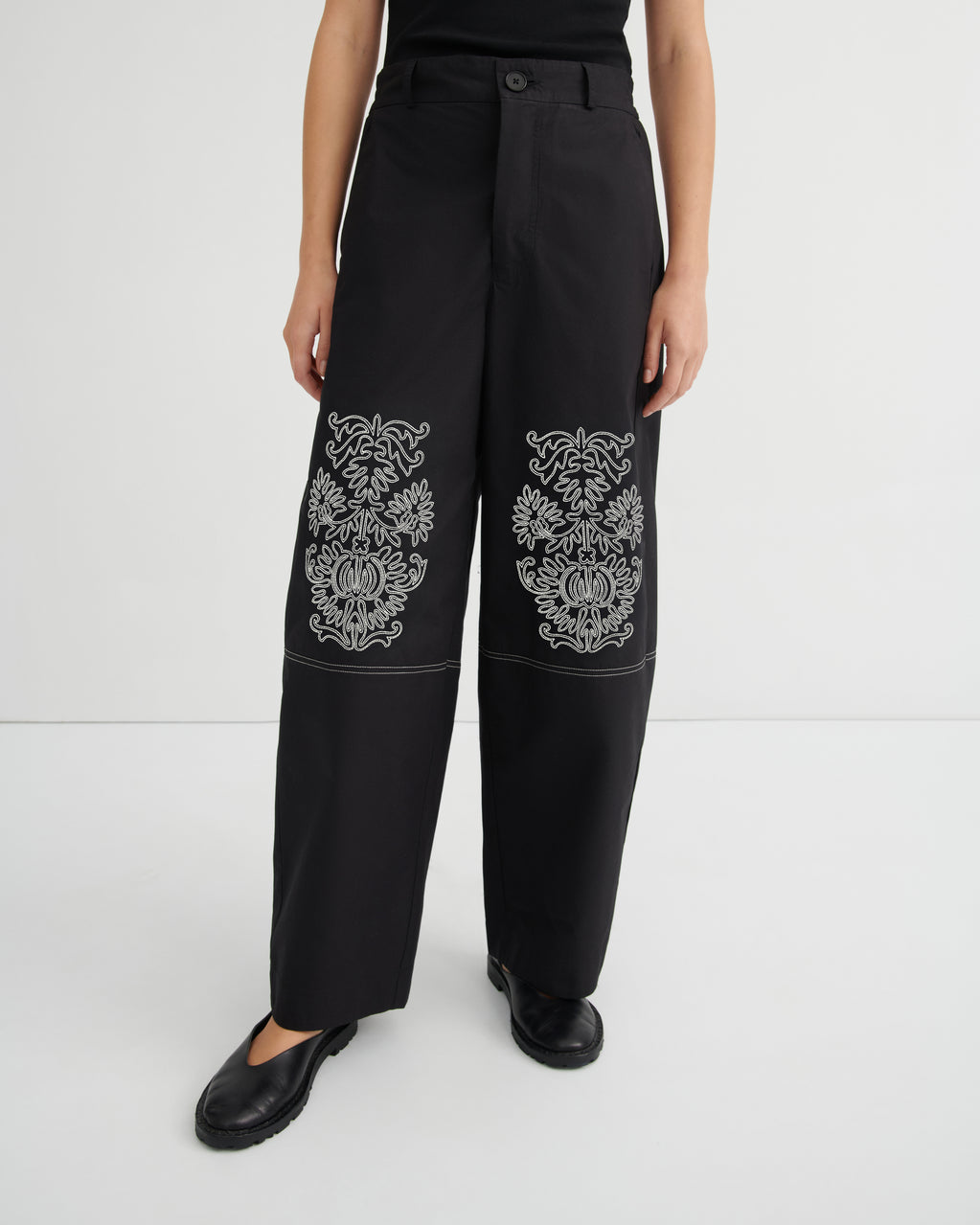 Black pants with white floral embroidery on a white background