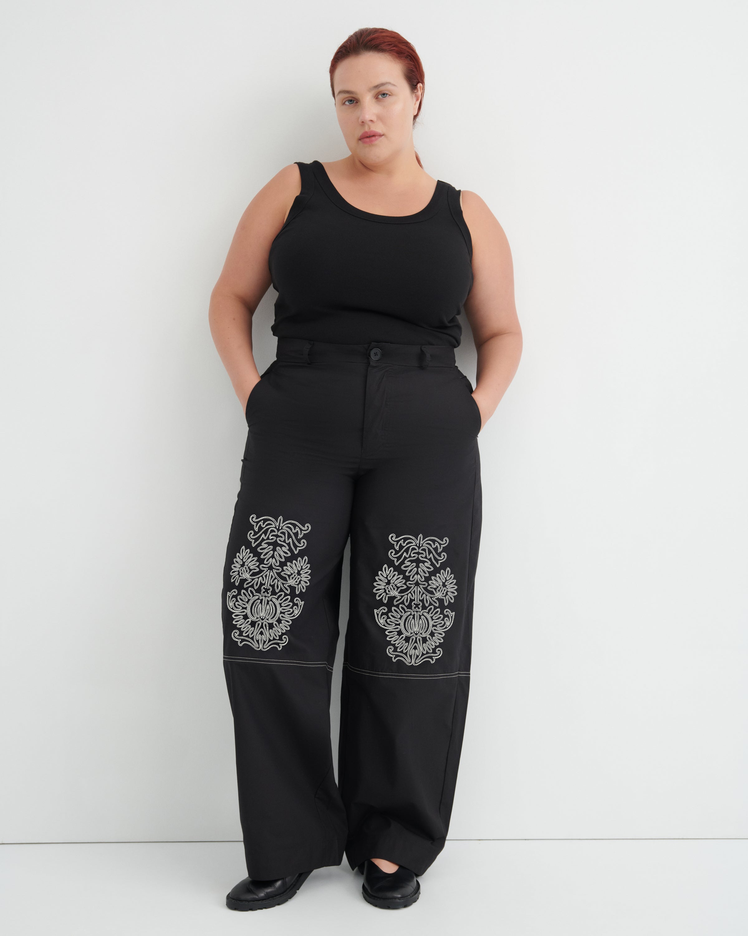 Person wearing black sleeveless top and pants with floral patterns on a white background