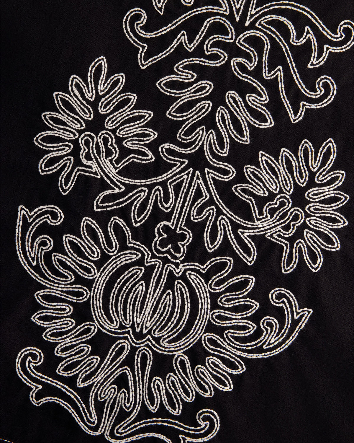Close-up of a black fabric surface with an ornate white embroidered floral and scroll pattern.
