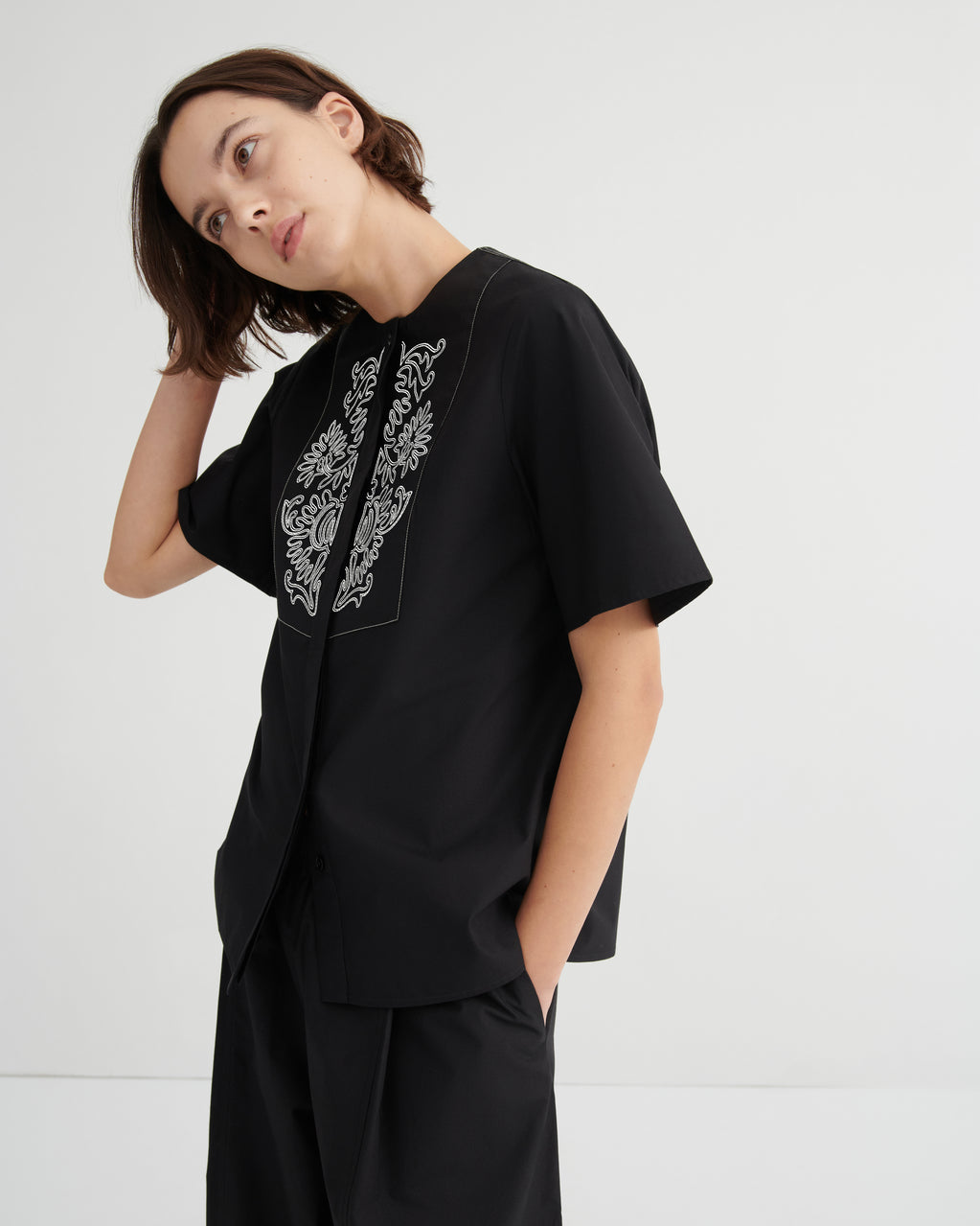 Person wearing a black outfit with white embroidery on a plain background