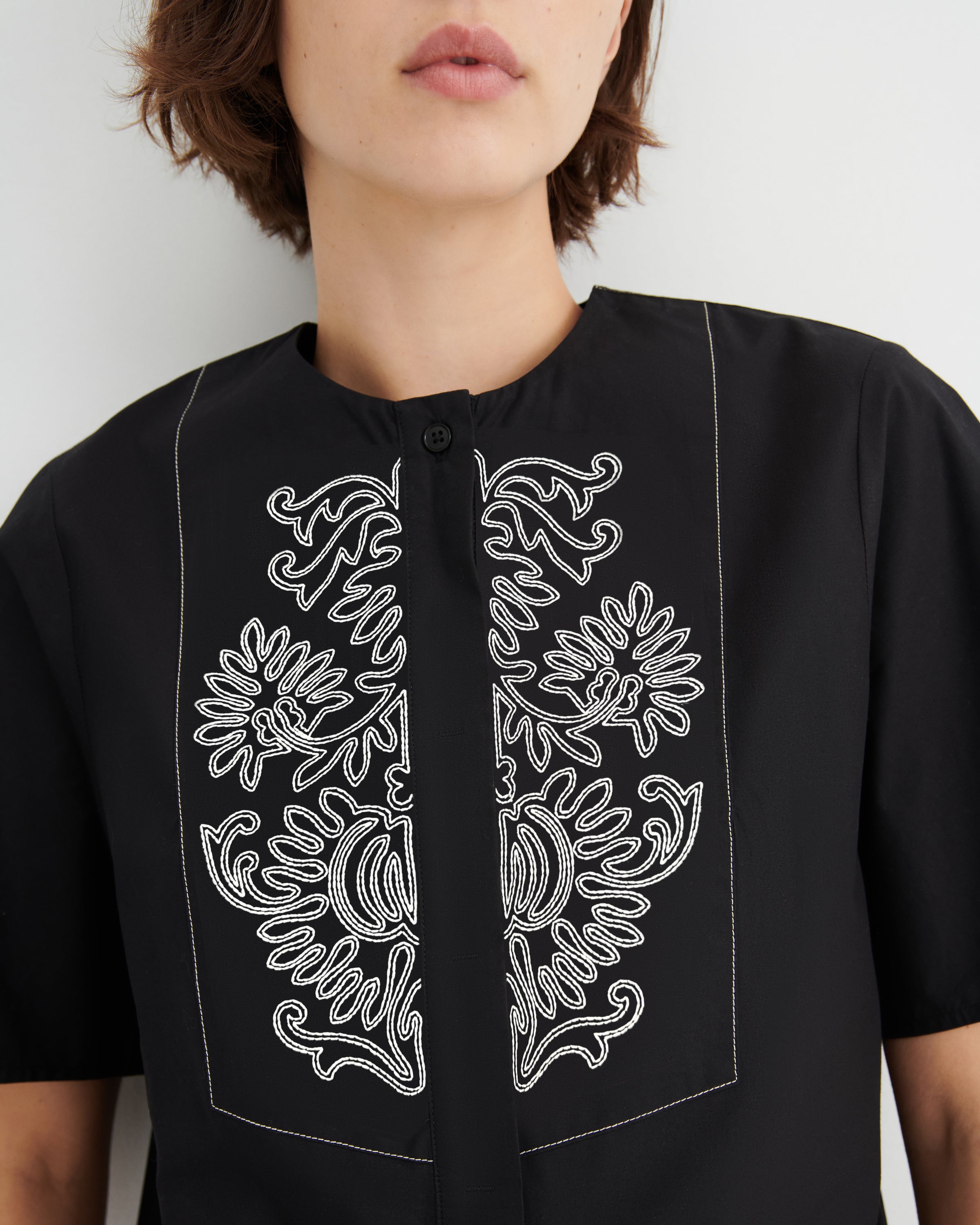 Black shirt with white floral embroidery on a plain background