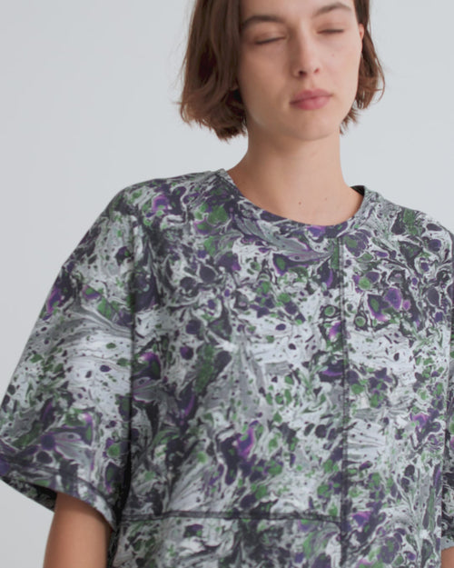 A women wearing a short sleeve tee and maxi skirt with a blue, green and purple abstract marbled print against a grey background.