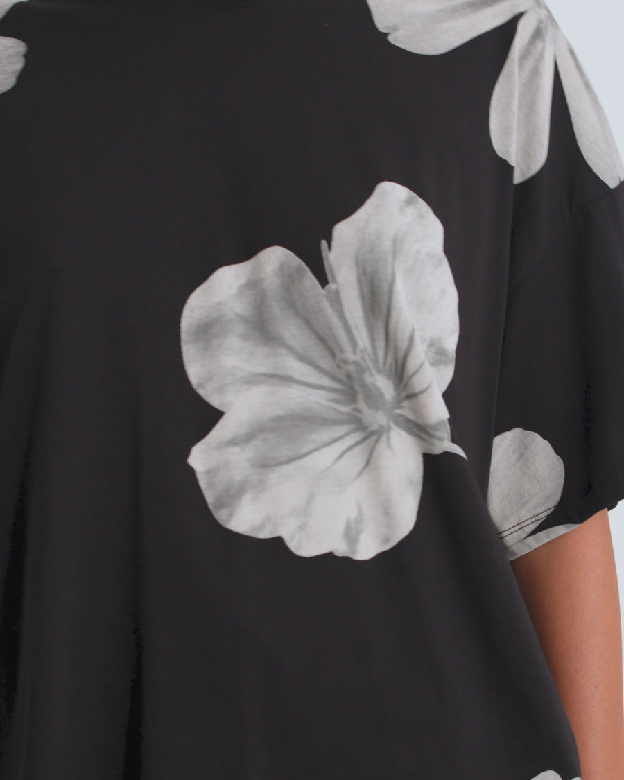 A women wearing a black oversized tee with white floral print and black shorts.