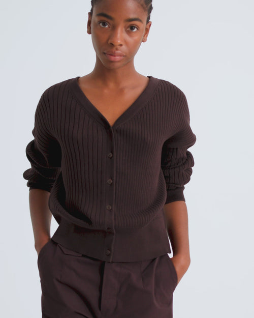 A women wears a brown v neck button up ribbed cardigan with rolled up sleeves and brown wide leg trousers.