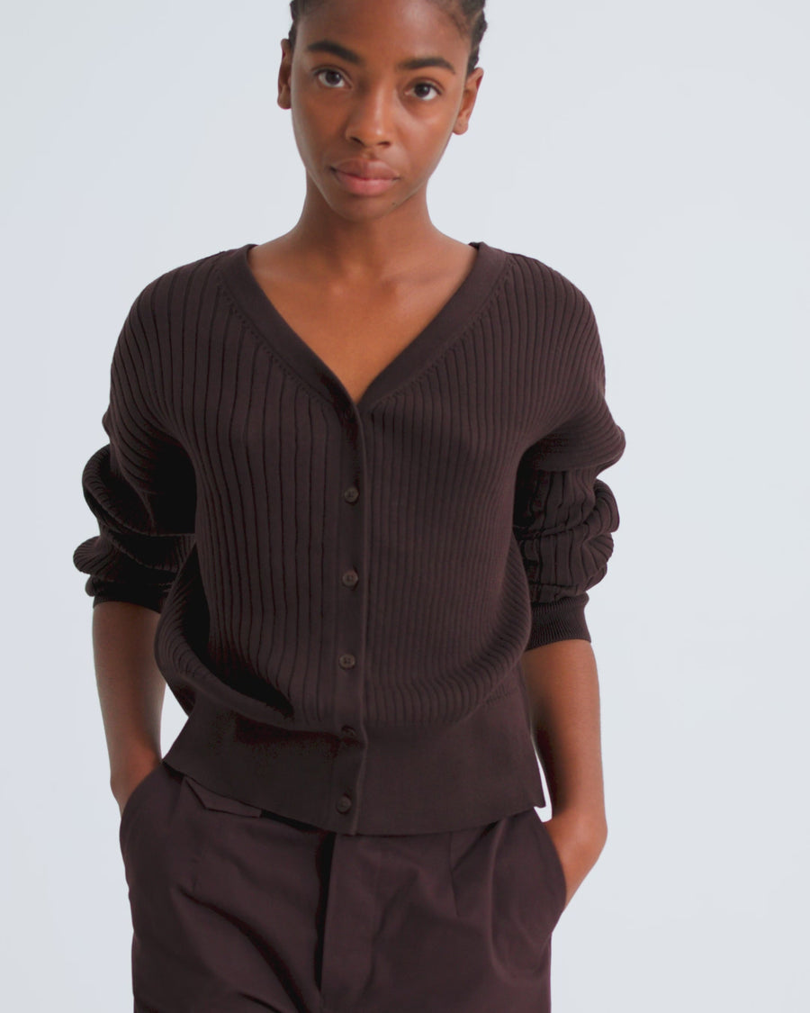 A women wears a brown v neck button up ribbed cardigan with rolled up sleeves and brown wide leg trousers.