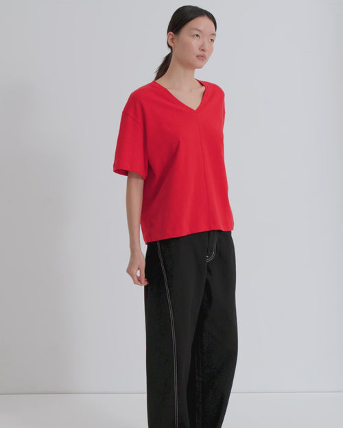 A women wears a red, oversized v-neck tee and black barrel leg jeans with white topstitching.