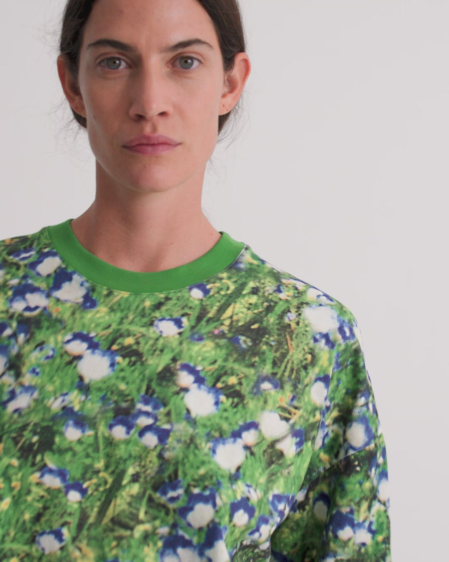 A women wearing an oversized boxy tee in a floral print with dark denim shorts against a grey background.