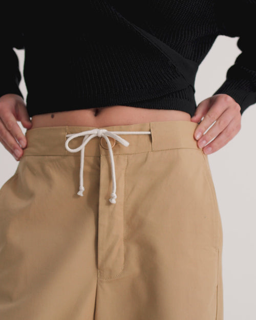A women wears relaxed tan pants and a fitted black wrap cardigan.