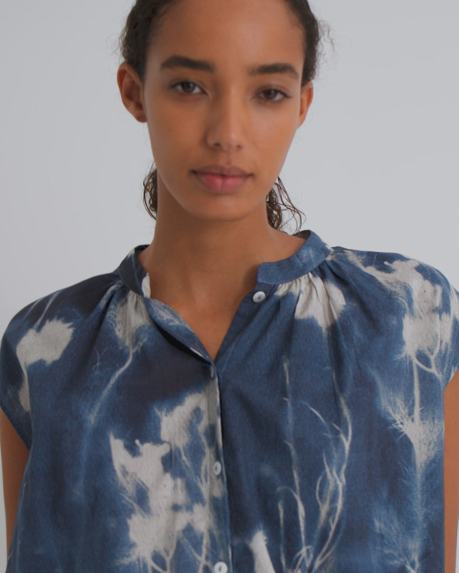 Woman wearing a blue and white floral top and navy denim shorts against a white background