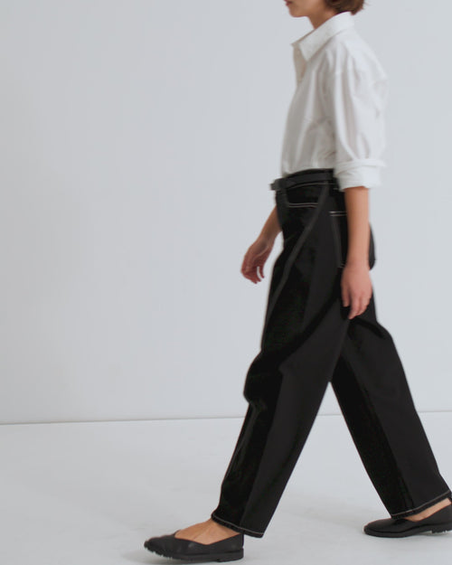 A women wears a white, button up shirt with the sleeves rolled up and black, barrel leg jeans with white topstitching and black flats.