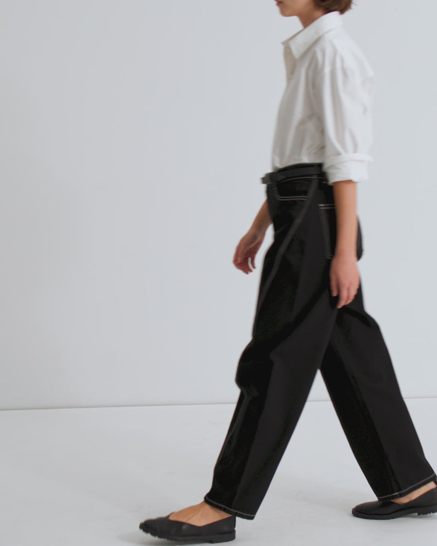 A women wears a white, button up shirt with the sleeves rolled up and black, barrel leg jeans with white topstitching and black flats.
