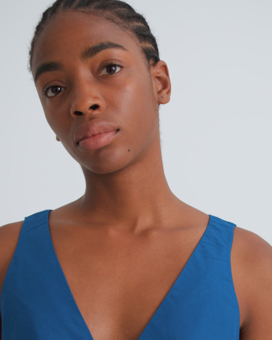 A model wearing a sleeveless, V-neck maxi dress in a vibrant royal blue, paired with brown leather shoes, standing against a plain white studio background.
