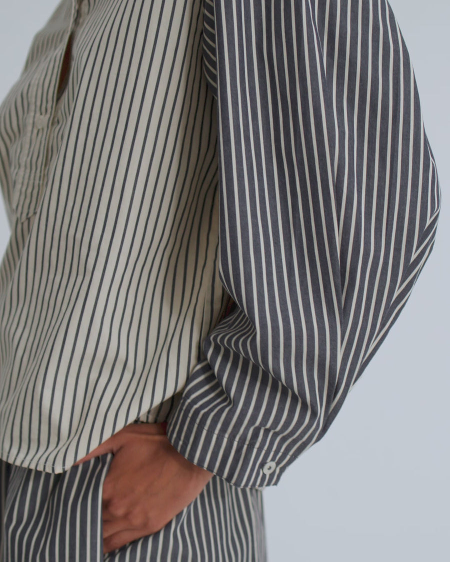 A women wearing a striped long sleeve shirt with match striped pleated shorts against a grey background.