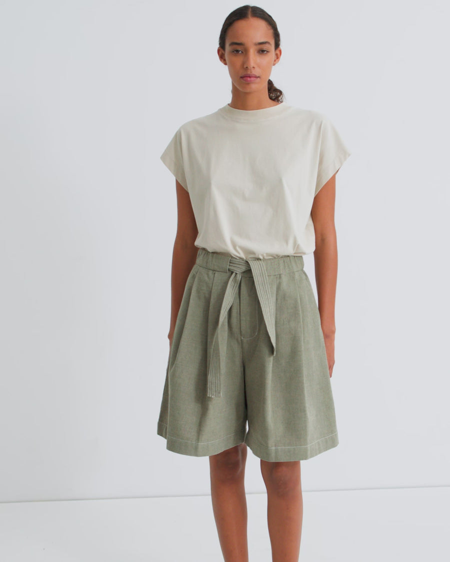 A women wearing an off white cap sleeve tee with high waisted belted sage green pleated shorts.