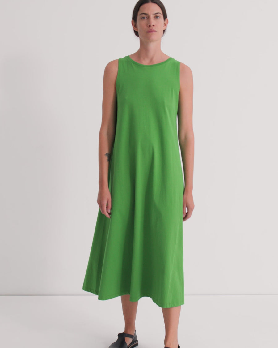 A women wearing a sleeveless green midi a-line dress against a grey background.