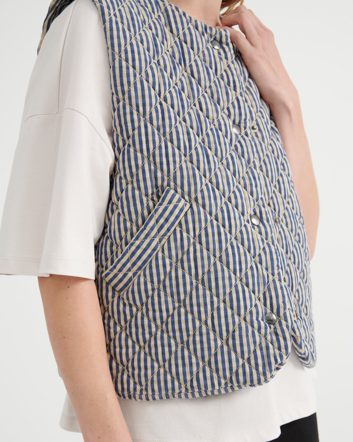 A close-up of a person wearing a blue and white gingham quilted vest over a white t-shirt, against a plain white background.