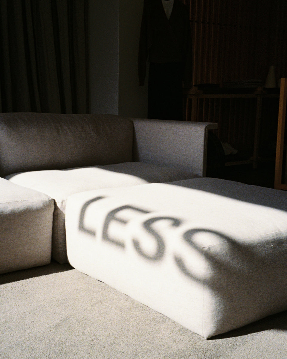 A shadowing photo of a grey couch with a sunspot with shadow letters that read 'LESS'